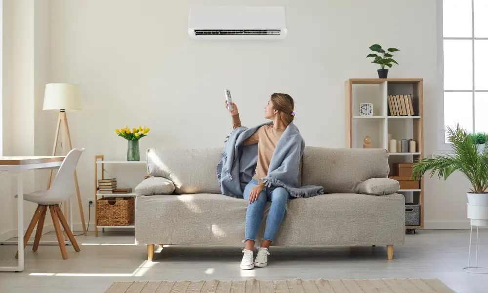 女性がソファーに座り、毛布をかけて HVAC システムを制御しています。